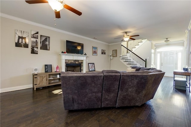 living room featuring ceiling fan, a stone fireplace, ornamental molding, and dark wood-type flooring