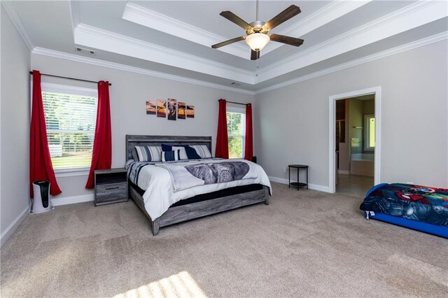 carpeted bedroom with ceiling fan, a raised ceiling, crown molding, and ensuite bathroom