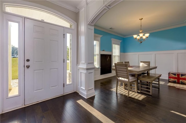 foyer entrance with a notable chandelier, decorative columns, crown molding, and dark hardwood / wood-style flooring