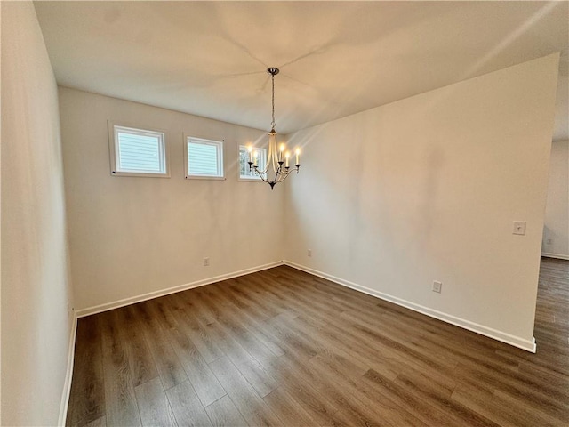 spare room featuring dark wood-style flooring, baseboards, and an inviting chandelier