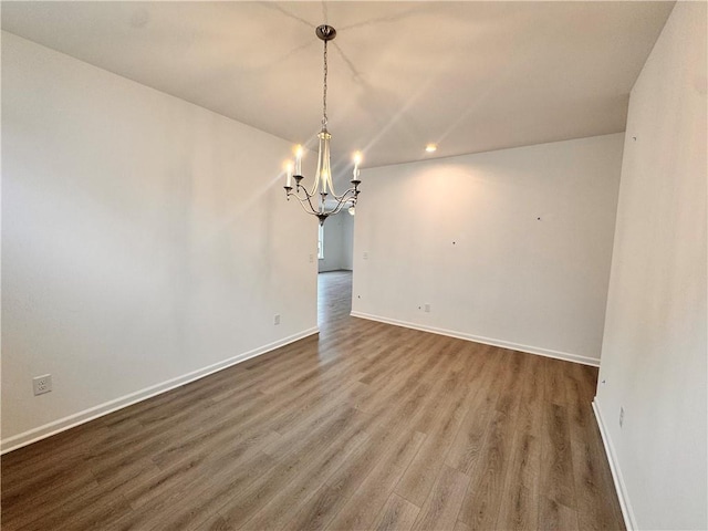 spare room featuring a chandelier, wood finished floors, and baseboards