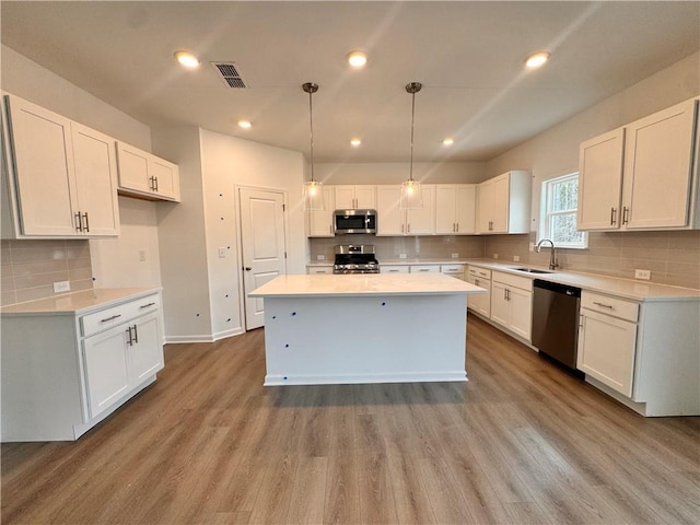 kitchen with a center island, stainless steel appliances, visible vents, a sink, and wood finished floors