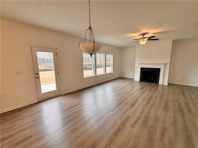 unfurnished living room with a ceiling fan, a fireplace, baseboards, and wood finished floors