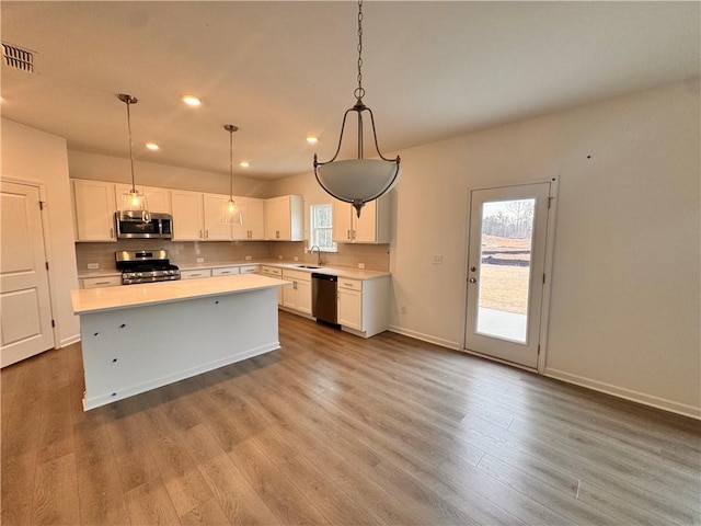 kitchen with stainless steel appliances, light countertops, backsplash, white cabinetry, and a sink