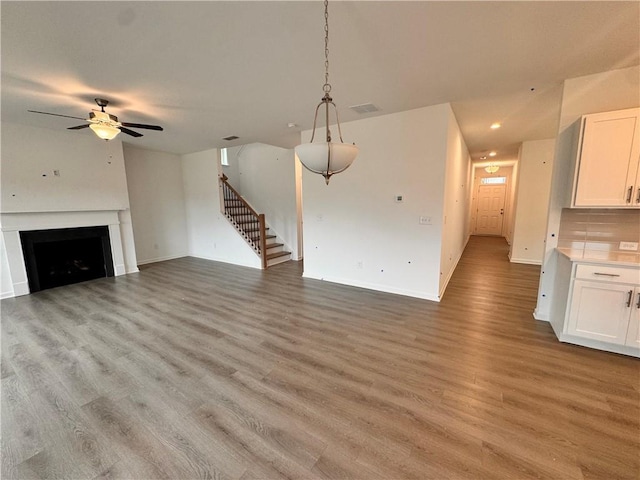 unfurnished living room featuring light wood-style flooring, a fireplace, visible vents, baseboards, and stairway