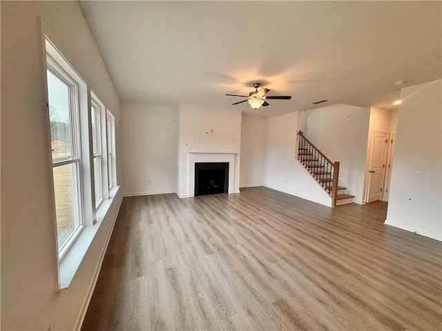 unfurnished living room featuring a fireplace, visible vents, wood finished floors, baseboards, and stairs