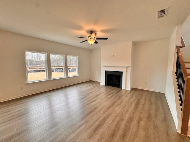 unfurnished living room with ceiling fan, a fireplace, wood finished floors, visible vents, and baseboards