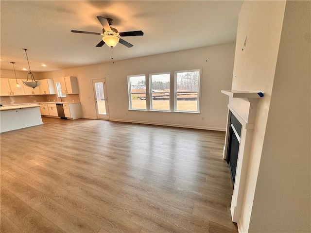 unfurnished living room featuring light wood-type flooring, ceiling fan, a fireplace, and baseboards