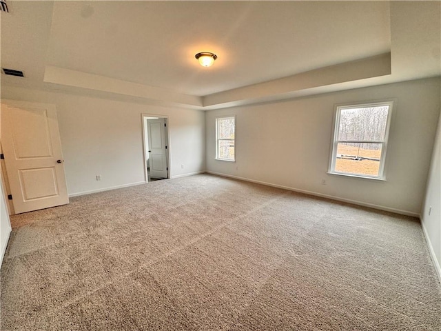 carpeted empty room featuring a raised ceiling, visible vents, and baseboards