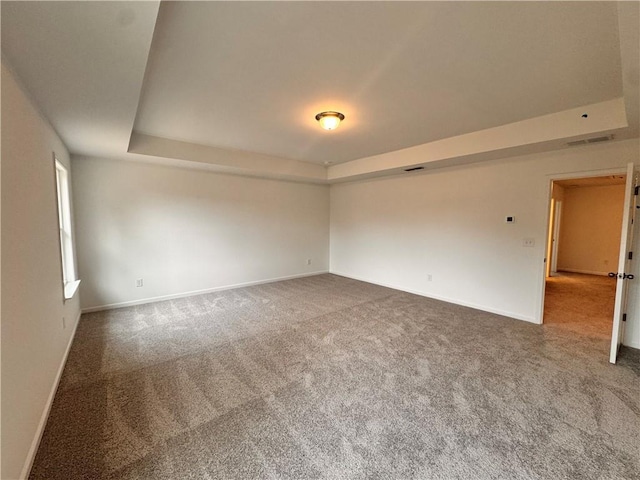 empty room featuring carpet floors, a raised ceiling, and baseboards