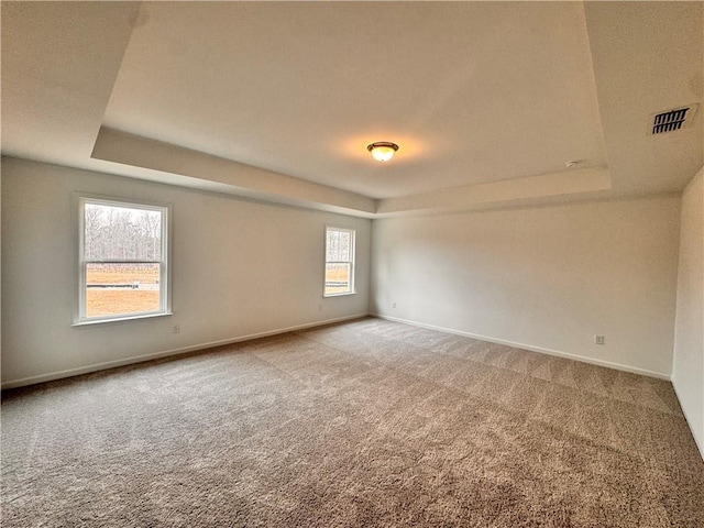 carpeted empty room featuring a tray ceiling, visible vents, and baseboards