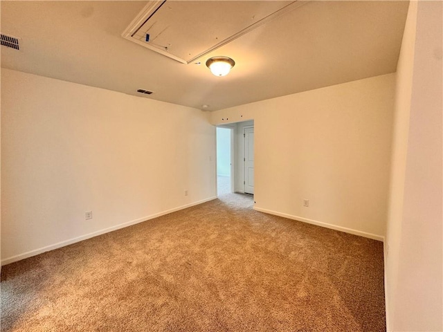 carpeted empty room with attic access, visible vents, and baseboards