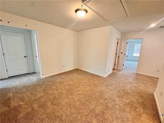 empty room featuring carpet floors, attic access, and baseboards