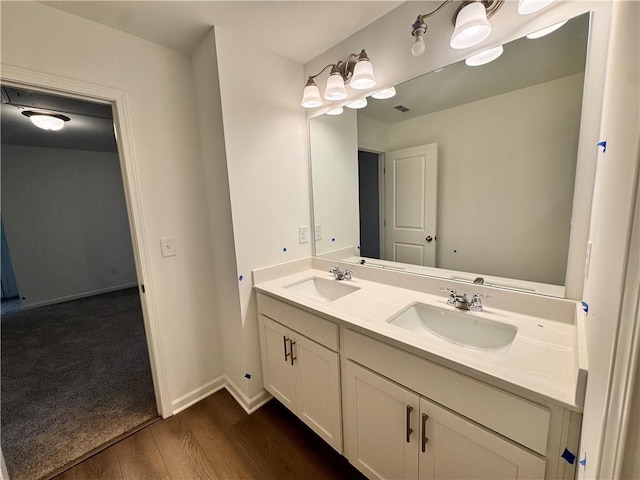 bathroom with double vanity, baseboards, a sink, and wood finished floors