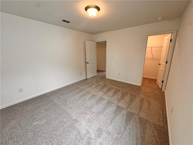 unfurnished bedroom featuring carpet flooring, visible vents, baseboards, a closet, and a walk in closet