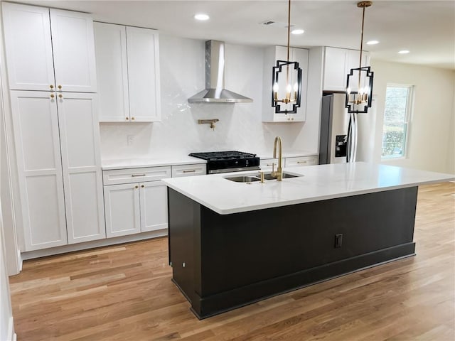 kitchen with wall chimney range hood, stainless steel fridge, an island with sink, and white cabinets