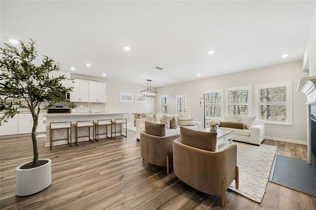 living area featuring light wood-type flooring, a fireplace with flush hearth, visible vents, recessed lighting, and baseboards