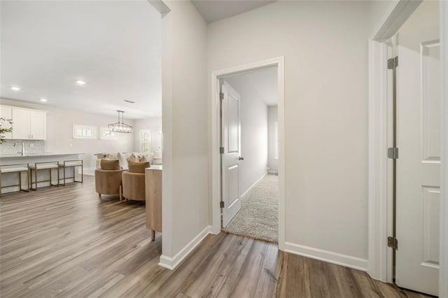 hall with recessed lighting, baseboards, light wood-type flooring, and a sink