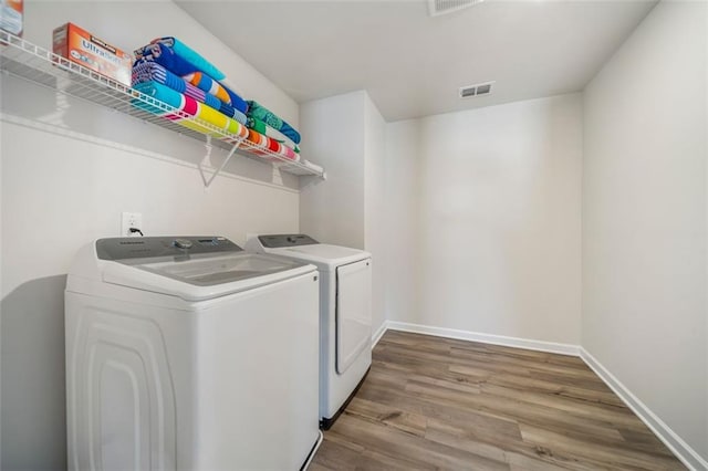 washroom with washing machine and clothes dryer, visible vents, baseboards, laundry area, and wood finished floors