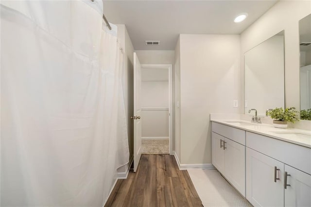 bathroom with wood finished floors, baseboards, visible vents, double vanity, and a sink