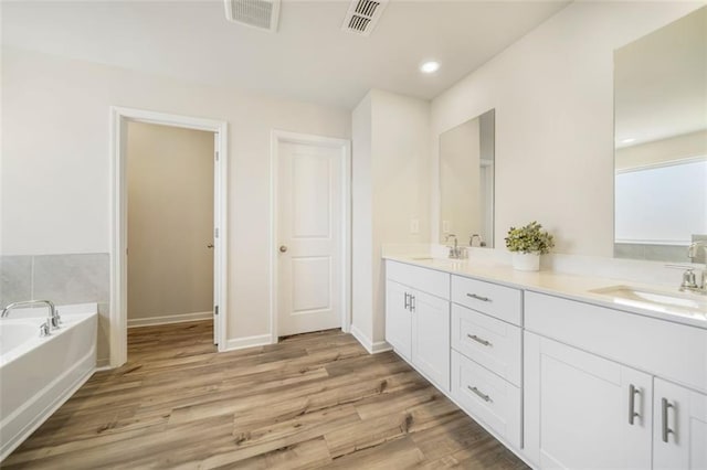 bathroom with a bath, wood finished floors, visible vents, and a sink