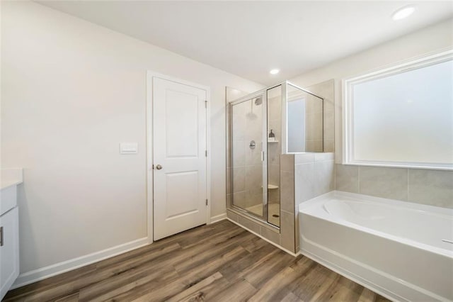 full bath featuring wood finished floors, a shower stall, baseboards, a bath, and vanity