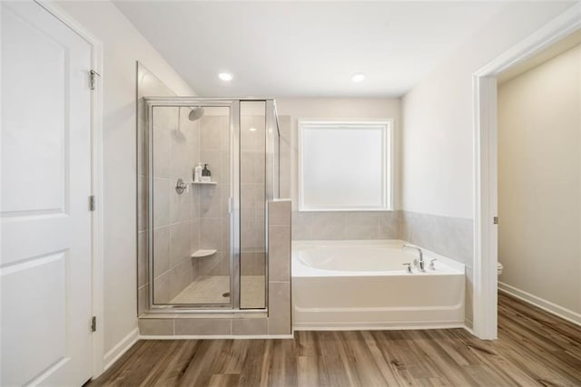 bathroom featuring a garden tub, toilet, wood finished floors, a shower stall, and baseboards