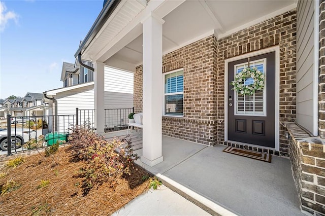 view of exterior entry featuring brick siding and a porch