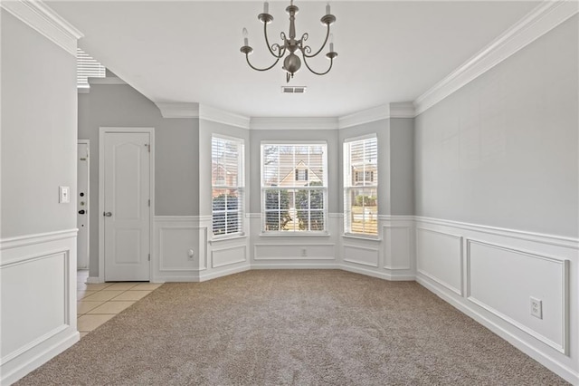 carpeted spare room with a decorative wall, a wainscoted wall, visible vents, ornamental molding, and an inviting chandelier