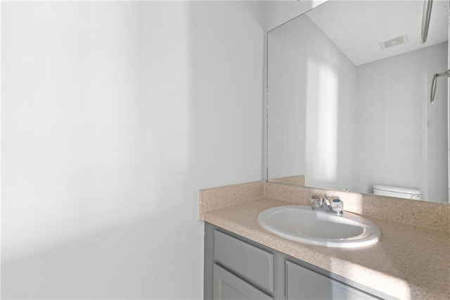 bathroom featuring toilet, vanity, and visible vents