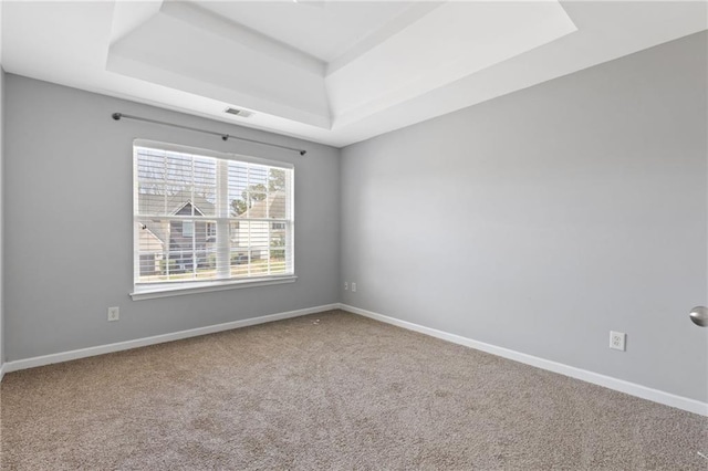 carpeted empty room with visible vents, baseboards, and a raised ceiling