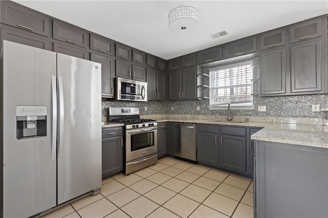 kitchen featuring light tile patterned floors, stainless steel appliances, a sink, backsplash, and light stone countertops