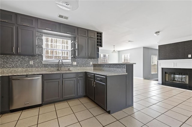 kitchen featuring light tile patterned flooring, a peninsula, a sink, backsplash, and dishwasher