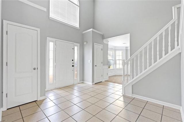 foyer entrance featuring stairs, light tile patterned floors, a towering ceiling, and baseboards