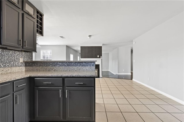 kitchen with light tile patterned floors, visible vents, backsplash, a peninsula, and baseboards