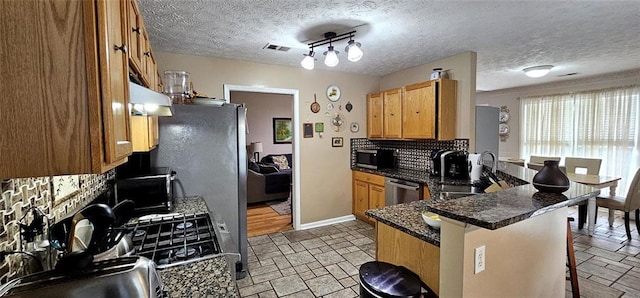 kitchen with dark stone countertops, a breakfast bar, backsplash, kitchen peninsula, and stainless steel appliances