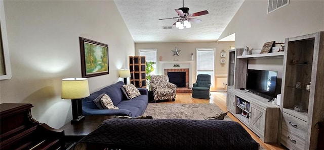 living room with vaulted ceiling, a fireplace, a textured ceiling, ceiling fan, and hardwood / wood-style floors