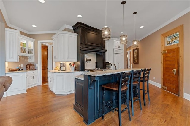 kitchen with white cabinets, an island with sink, crown molding, pendant lighting, and light wood-type flooring