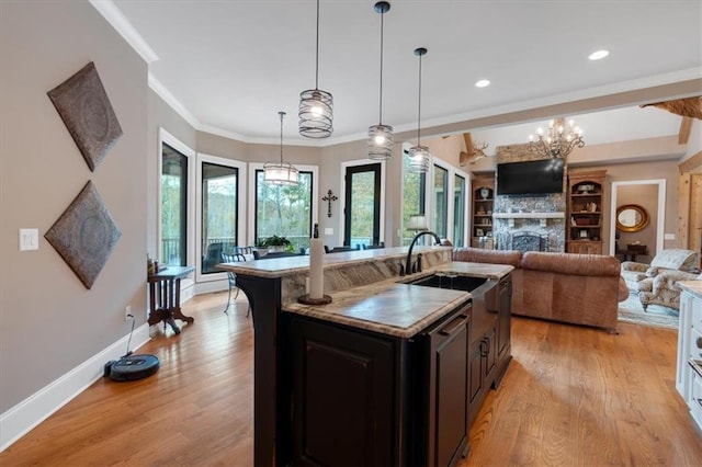 kitchen with light hardwood / wood-style floors, a center island with sink, hanging light fixtures, ornamental molding, and beamed ceiling