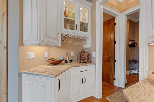 bar with white cabinetry, light stone countertops, and light wood-type flooring