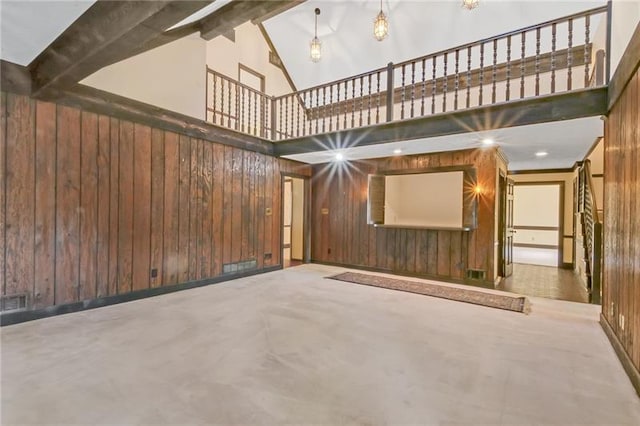 unfurnished living room with a towering ceiling, beam ceiling, and wooden walls
