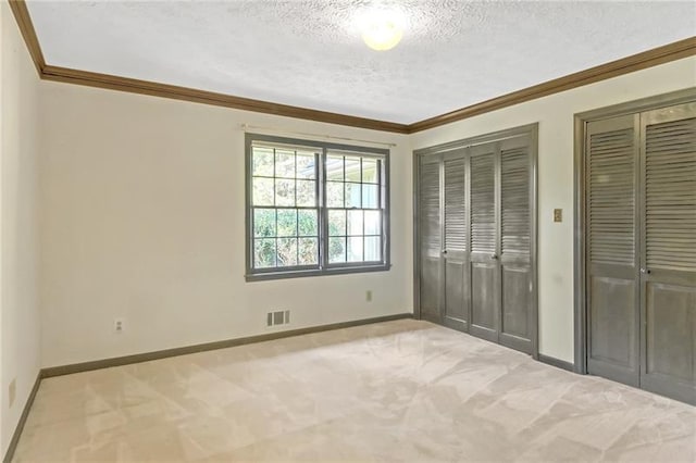 unfurnished bedroom featuring a textured ceiling, visible vents, crown molding, baseboards, and two closets