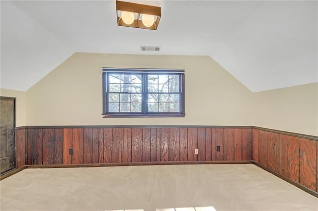 additional living space with carpet floors, wood walls, a wainscoted wall, and vaulted ceiling