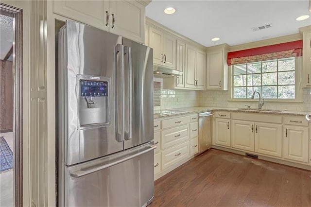 kitchen featuring a sink, stainless steel appliances, decorative backsplash, wood finished floors, and under cabinet range hood