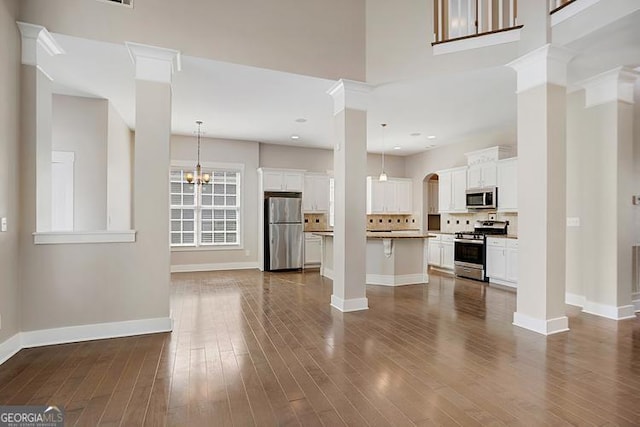 unfurnished living room featuring ornate columns, dark wood-style floors, baseboards, and a towering ceiling