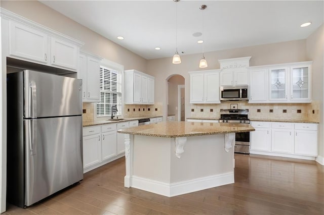 kitchen with white cabinets, arched walkways, backsplash, a kitchen island, and appliances with stainless steel finishes