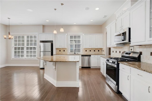 kitchen with a sink, an inviting chandelier, baseboards, appliances with stainless steel finishes, and a kitchen island
