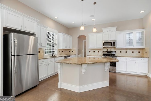 kitchen featuring a kitchen island, dark wood-type flooring, arched walkways, white cabinets, and stainless steel appliances