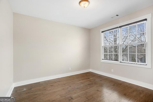 spare room with visible vents, baseboards, and dark wood-style flooring