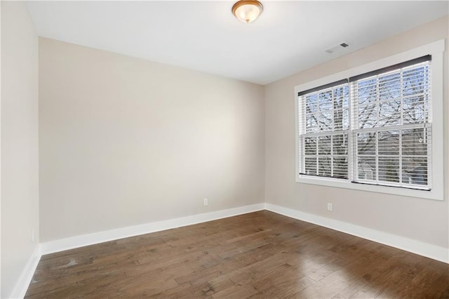 unfurnished room with baseboards, dark wood-type flooring, and visible vents
